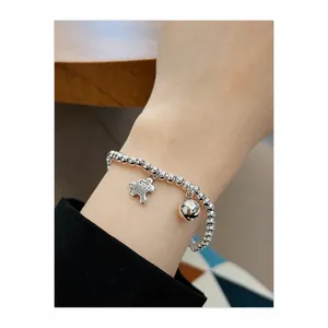 Detail eines silbernen Perlenarmbands mit Puzzle- und Glockenanhänger am Handgelenk