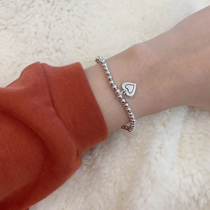 Detailansicht der silbernen Perlenarmband mit Herzanhänger auf weißem Stoffhintergrund