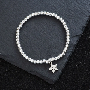 Poliertes Silberperlen-Armband mit lächelndem Sternanhänger auf dunklem Schieferhintergrund
