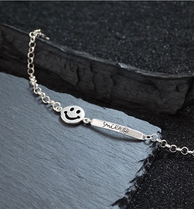 Detail of silver chain bracelet with smile pendant and engraved smile bar on dark rock