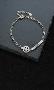 Detail of silver smile pendant bracelet on dark stone with engraved Smile bar charm