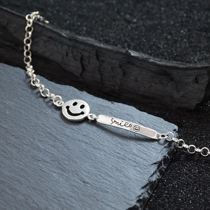 Chic silver smile face pendant bracelet with engraved bar on dark aesthetic background