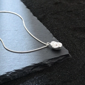 Elegant silver peanut pendant necklace with white pearl on a dark stone background