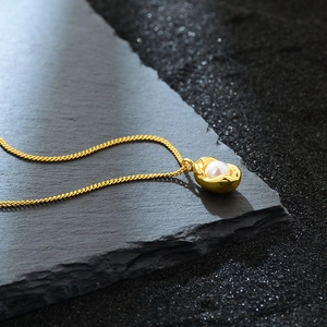 Elegant gold necklace featuring a peanut-shaped pendant with a white pearl on stone