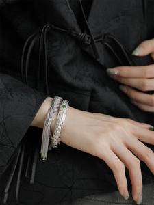 Détails de bracelets en argent tissés avec pierre de jade verte et pompons sur le poignet