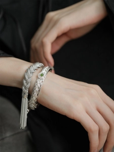 Détail d'un bracelet tressé argenté avec jade vert et de longs pompons élégants