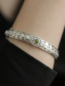 Détail d'un bracelet tissé en métal argenté orné d'une pierre précieuse vert émeraude