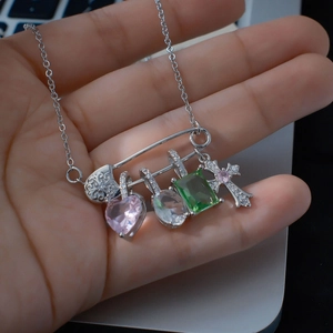 Collier trombone argenté avec breloques cœur et croix colorées porté à la main
