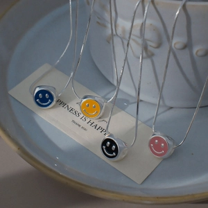 Détail de pendentifs smiley en émail coloré bleu, jaune, noir et rose sur chaînes argentées