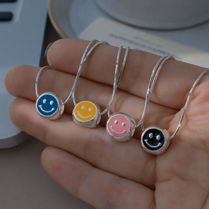 Détail de pendentifs smiley en émail coloré sur chaînes serpent argentées en main