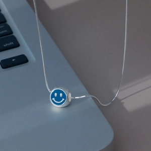 Détail du pendentif smiley bleu en émail sur chaîne serpent argentée sur ordinateur