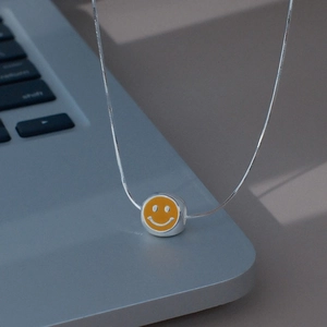 Détail d'un pendentif sourire en émail jaune sur chaîne argentée sur un clavier de PC