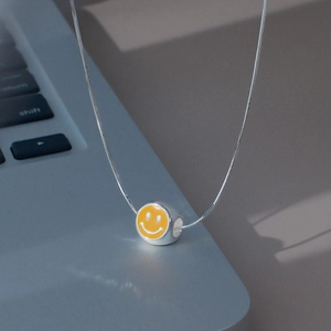 Détail du pendentif smiley en émail jaune avec chaîne argentée sur fond d'ordinateur