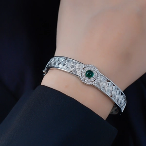 Close-up of woven silver bracelet featuring a green gemstone and white diamond halo