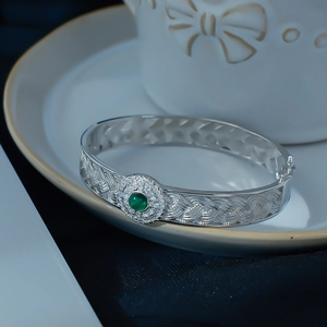 Macro shot of silver woven bracelet with a green gemstone and sparkling white stones