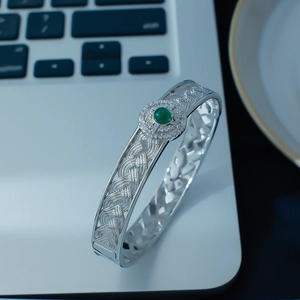 Detail of woven texture silver bangle with a centered green gemstone and white crystal inlay