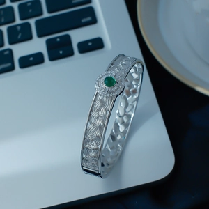 Detail of silver lace cuff bracelet featuring a green gemstone and sparkling zircons
