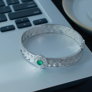 Detail of silver woven bracelet with green gemstone inlay on a sleek silver background