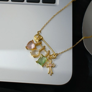 Close-up of safety pin necklace with colorful zircon heart, cross, and emerald pendants