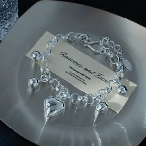 Detail eines silbernen Herzanhänger-Armbands mit polierten Perlen und Gliederkette