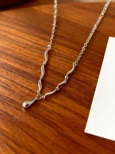 Dettaglio della collana argentata con ciondolo a goccia e maglie ondulate su legno