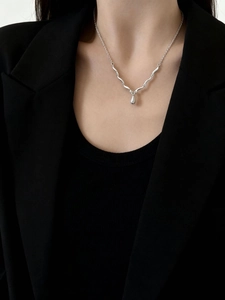 Dettaglio di una collana in argento con pendente a goccia indossata su un abito nero