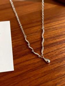 Dettaglio della collana minimalista in argento con ciondolo a goccia su base in legno