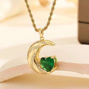 Macro detail of gold moon pendant with heart green crystal and twisted rope chain