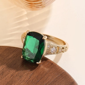 Close-up of emerald-cut green crystal ring with gold textured band and zircon accents