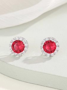 Primo piano di eleganti orecchini a lobo rotondi in zircone rosso e alone argento
