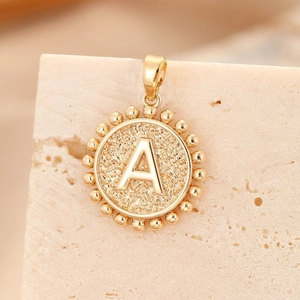 Polished gold round alphabet A pendant with beaded border on a rustic stone background