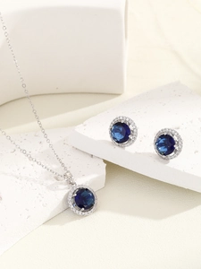 Detail of blue sapphire zircon pendant necklace and stud earrings set on marble stone