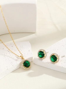 Close-up of golden jewelry set with emerald green stones and zircon accents on marble