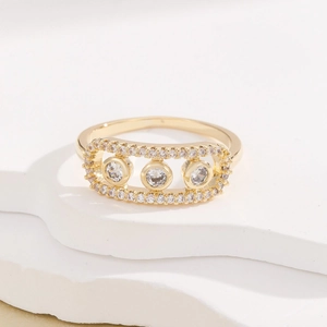 Elegant gold oval ring with hollow frame and three central stones on stone background