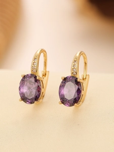 Macro shot of gold earrings featuring large oval purple gemstones and zircon accents