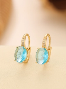 Close-up of gold hoop earrings with large oval light blue gemstones and small pavé diamonds