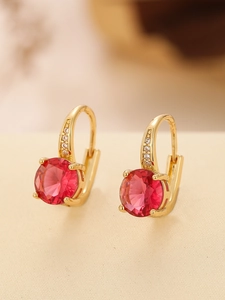 Close-up of gold earrings featuring a round red ruby zircon and small white crystals