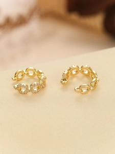 Close-up of golden Cuban chain ear cuff with cubic zirconia micro-pave on beige texture