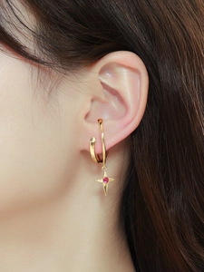 Primo piano di un ear cuff dorato con ciondolo a stella in zircone rosso all'orecchio