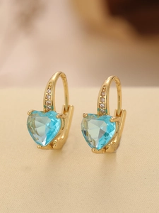 Close-up of golden hoop earrings featuring heart-shaped light blue gemstones and diamonds