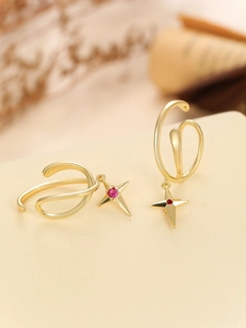 Dettaglio di ear cuff dorati con pendente a stella in zircone rosso su fondo beige
