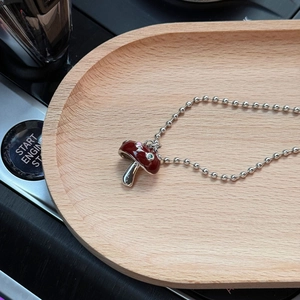 Détail du pendentif champignon en émail rouge avec pois sur une chaîne à billes