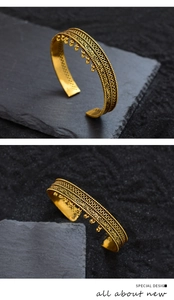 Makro-Detail des ethnischen Gold-Armreifs mit floralen Schnitzereien und Quastenperlen