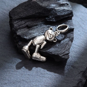 Colgante de oso articulado de plata con zapatillas de pedrería sobre fondo de carbón