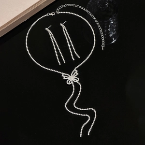 Close-up of butterfly bow jewelry set with tassel earrings on black mirror surface