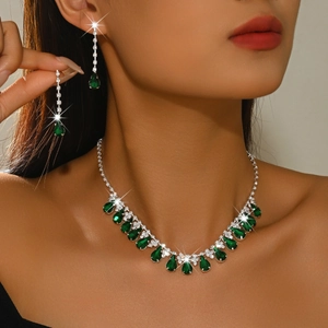 Macro detail of bridal jewelry set featuring pear-cut emerald gemstones and silver fringes