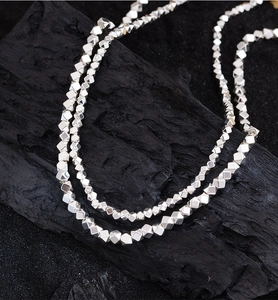 Macro view of silver faceted cube beads necklace on a textured black charcoal backdrop
