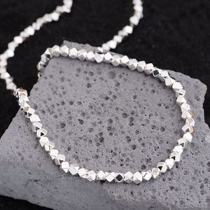 Minimalist silver geometric polyhedron bead necklace displayed on a dark volcanic rock