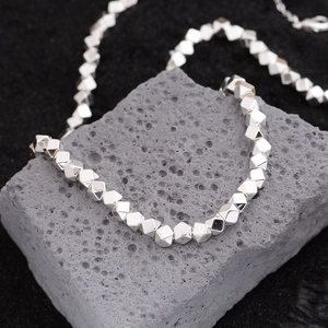 Minimalist silver cube bead necklace displayed on a textured volcanic stone background