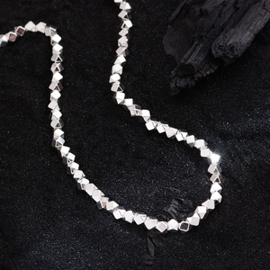 Minimalist silver faceted bead necklace displayed on black sand with charcoal accents